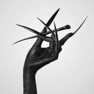 Black-painted hand with extremely long pointed stiletto nails holding makeup brushes against gray background