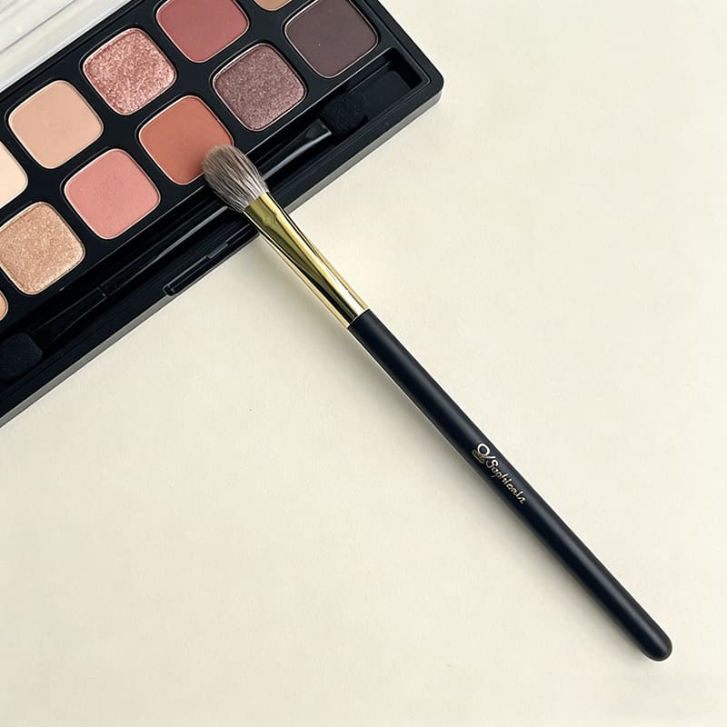 Eyeshadow palette with neutral pink and mauve shades next to sophienia makeup blending brush with black handle and gol...