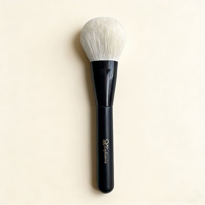 Sophienia makeup powder brush with soft white bristles and sleek black handle on cream background
