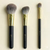 Three Sophienia makeup brushes in graduated sizes with gray bristles, gold ferrules, and black handles on cream background