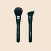 Two Sophienia makeup brushes with black handles - a round powder brush and an angled contour brush on beige background