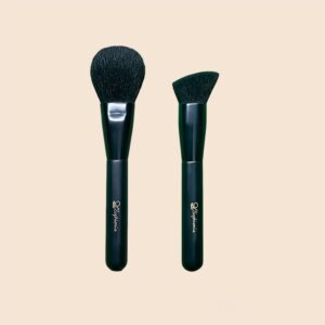 Two Sophienia makeup brushes with black handles - a round powder brush and an angled contour brush on beige background